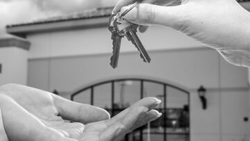 keys handed over in close-up to someone with building they have bought in background